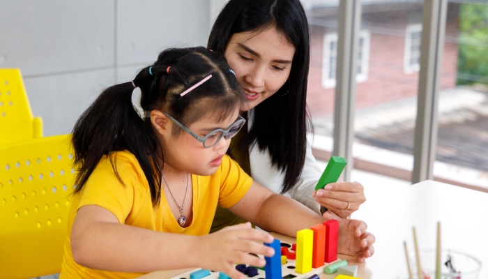 Asian girl with Down's syndrome play puzzle toy with her teacher in classroom.