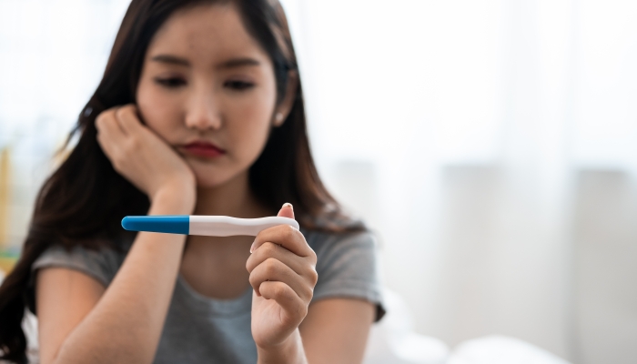 Asian woman sitting bed feeling disappointed when see the pregnancy test result.