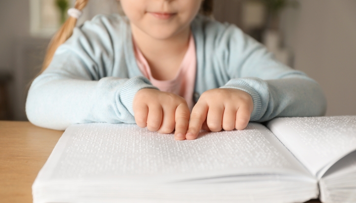 Blind child reading book written in Braille at table, closeup.