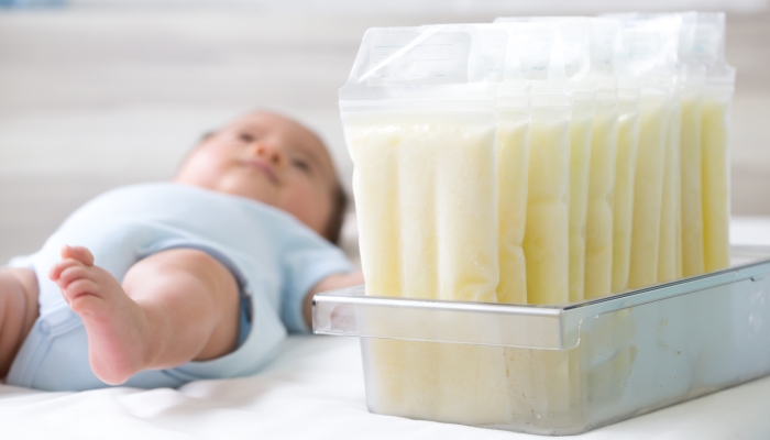 Breast milk frozen in storage bag and baby lying on background.