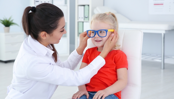 Children's doctor putting glasses on little girl in clinic.