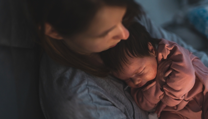 Close up portrait of newborn cute caucasian baby girl or boy in hands of mother putting to sleep at night.