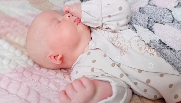 Cute baby rubs his eyes in his sleep with his hand.