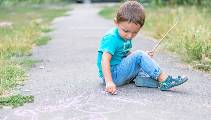 Cute kid boy drawing with chalk on the pavement in the park.