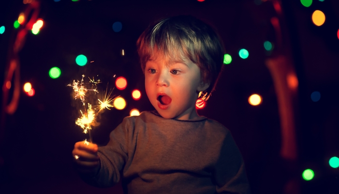 Cute little boy with a funny face holding sparklers.