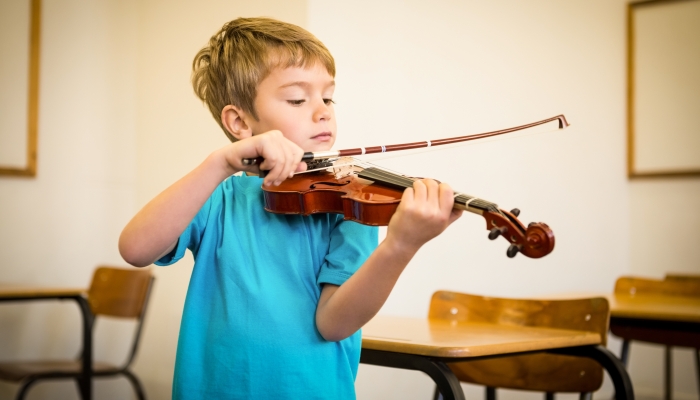 Cute pupil playing violin in classroom at the elementary school.