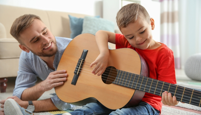 Father teaching his little son to play guitar at home.