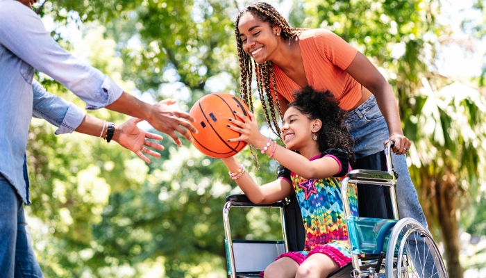 Girl in a wheelchair playing basketball with her family.