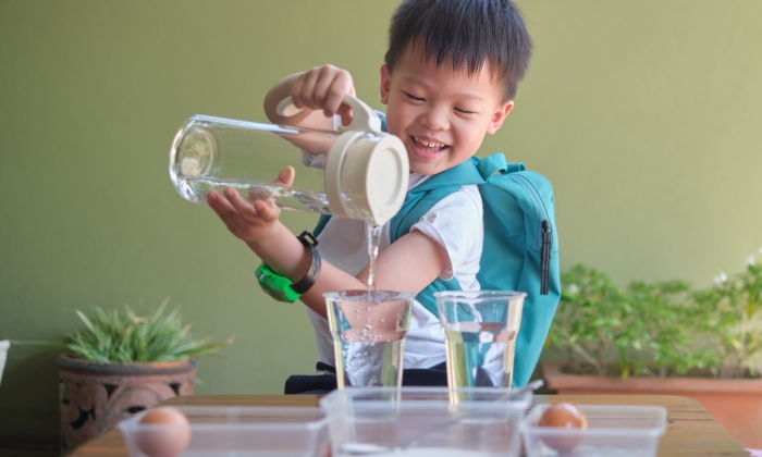 Happy Asian school kid studying science, pouring water to do fun and easy Floating Egg Science Experiment.