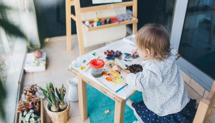 Happy cute toddler girl painting with gouache and watercolor paints on the balcony.