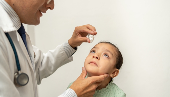 Ophthalmologist or pediatrician doctor putting eye drops into little girl's eye.