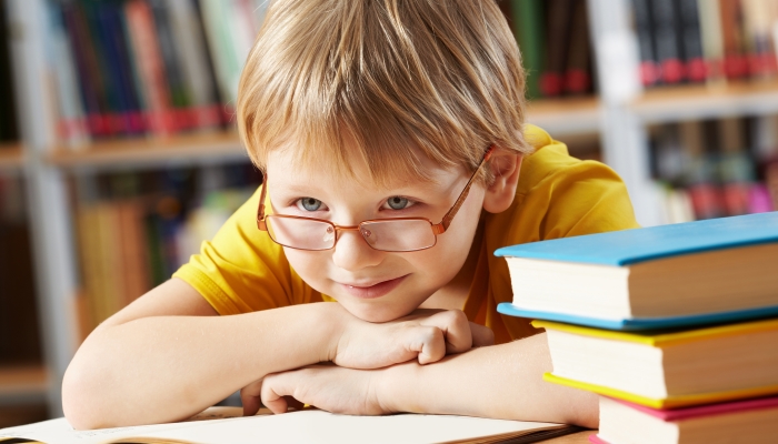 Portrait of clever boy with open book in library.