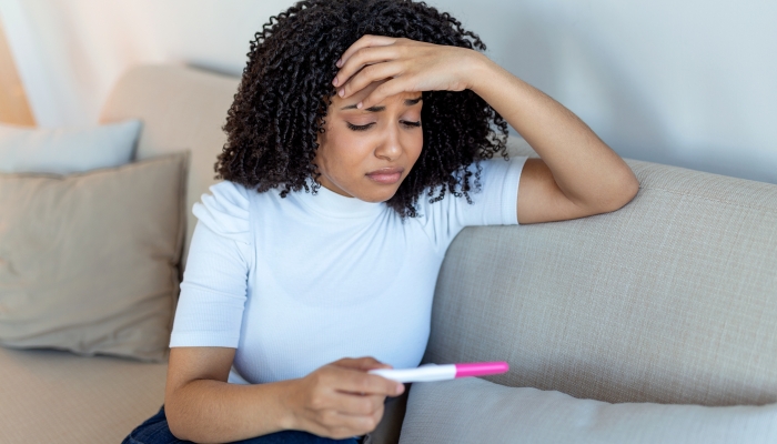 Sad, worried african american woman checking her recent pregnancy test.