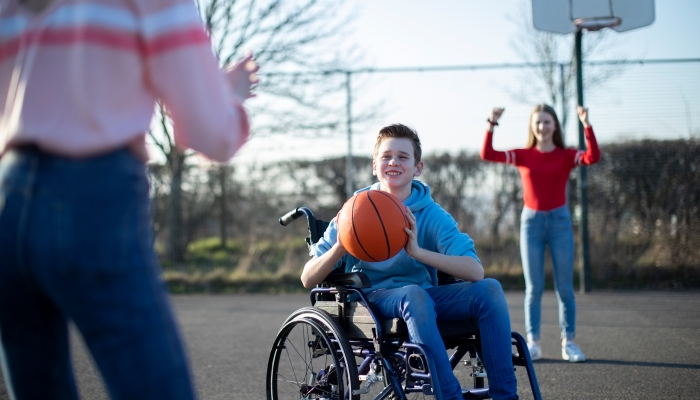 Teenage Boy In Wheelchair Playing Basketball With Friends.