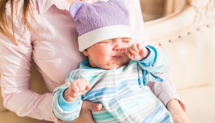 Tired newborn baby boy rubbing eyes.