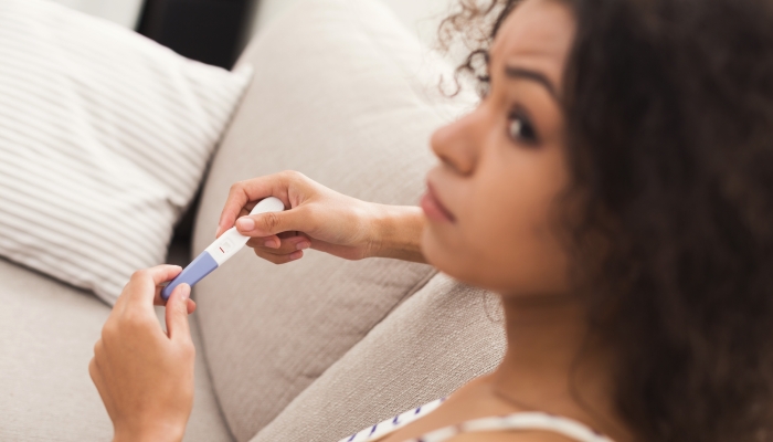 Worried african-american girl checking her recent pregnancy test.