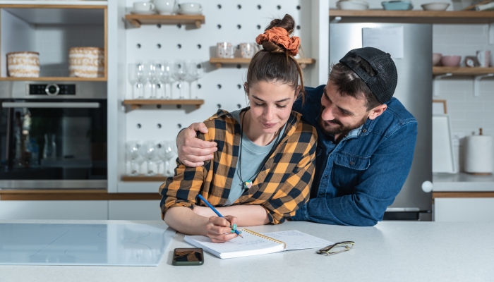 Young happy couple standing in the kitchen making a list of groceries they need to buy.