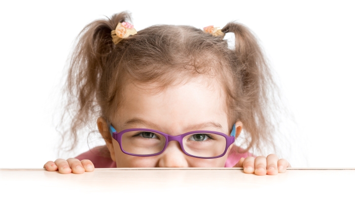 Frightened kid in spectacles looking from under table desk.