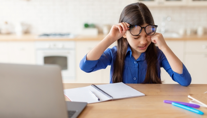 Tired Schoolgirl Rubbing Sore Eye Doing Homework On Laptop.