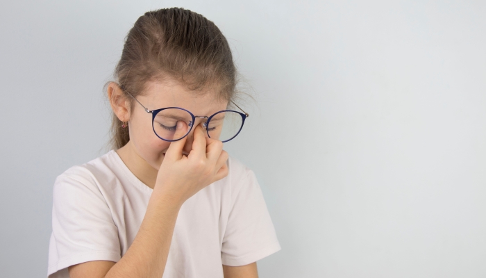 Little girl wipes tired eyes from glasses.