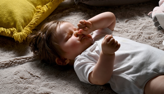 Portrait of a young baby lying on his back and rubbing his eyes.