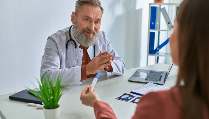 Serious grey bearded doctor looking carefully at female patient showing pregnancy test.