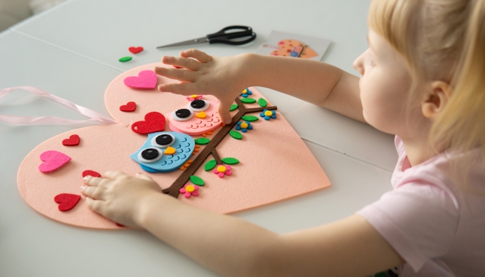 A blogger girl makes a felt craft for Valentine's Day in the shape of a heart.