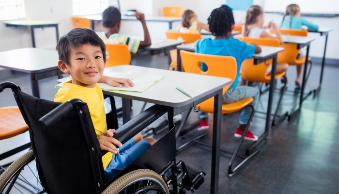 A cute people in wheel chair looking at the camera in classroom.