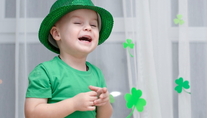 A little cheerful boy in a shiny green top hat and green clothes laughs.
