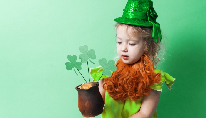 A little girl in a hat holds a small clay pot with gold coins.