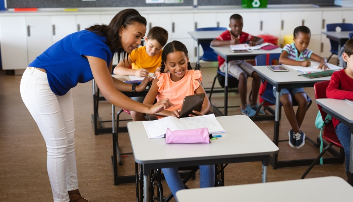 African american female teacher teaching disabled girl to use digital tablet at elementary school.