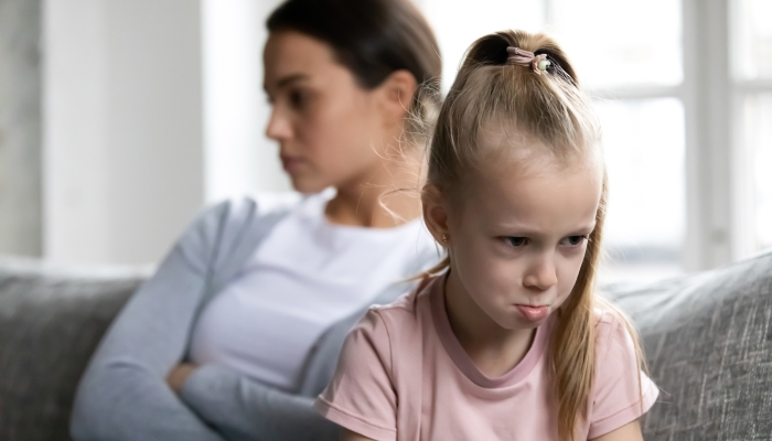 Annoyed upset quiet caregiver and kid sit on couch separately after arguing and quarrel.