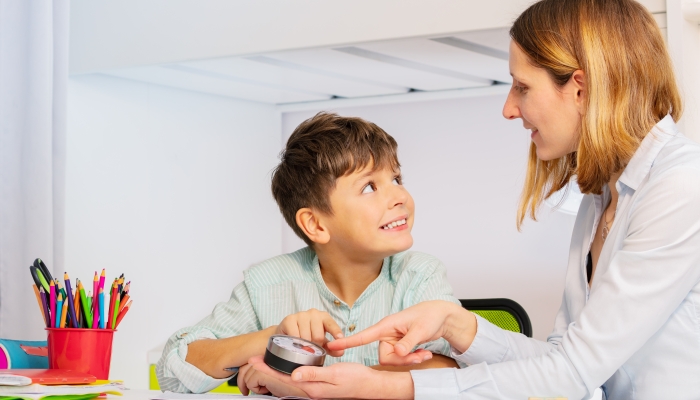 Autistic boy during ABA therapy look at teacher pointing to lesson timer.