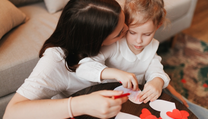 Beautiful young mother and her daughter make heart shaped cards for Valentine's day.