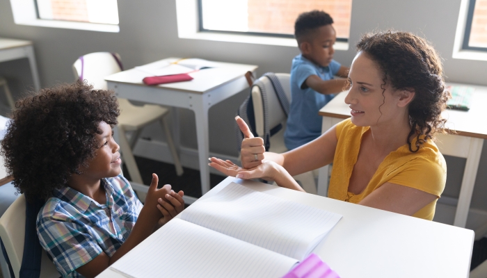 Caucasian young female teacher teaching sign language to african american elementary boy in class.