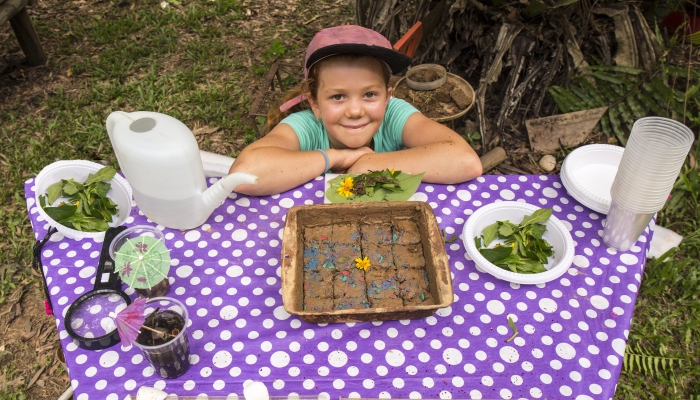 Child with mud cake and other party items outside playing.