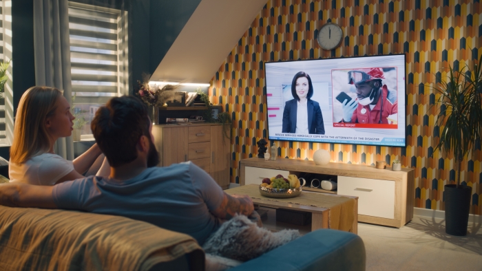 Couple sitting on sofa in living room together, talking, watching TV news.