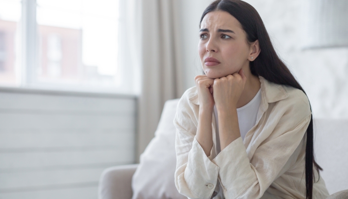 Depressed woman near window sitting on sofa.