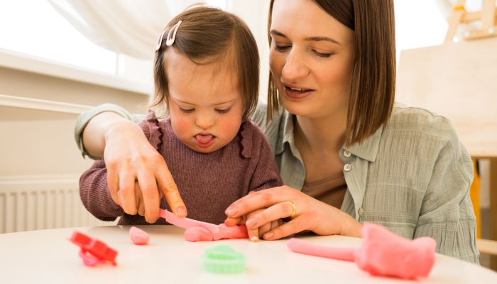 Girl with down syndrome sculpturing from the plasticine at the table.