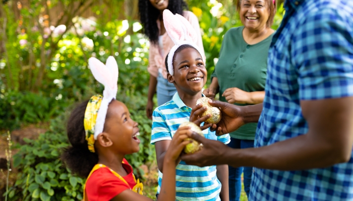 Happy african american siblings in bunny ears giving easter eggs to father in backyard.