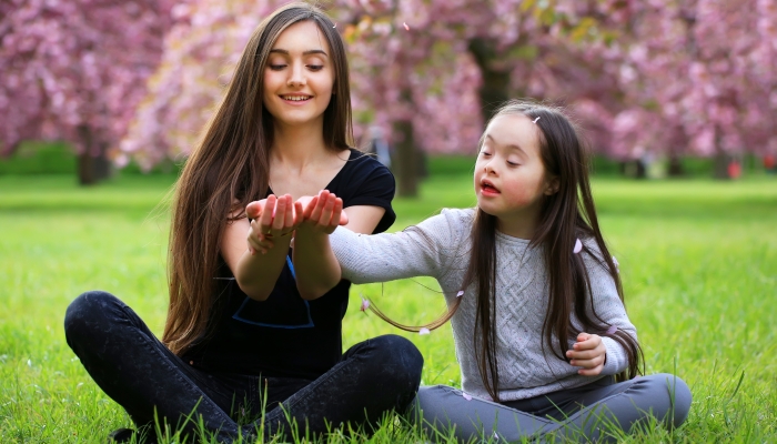 Happy beautiful young woman with girl in blossom park with trees and flowers.