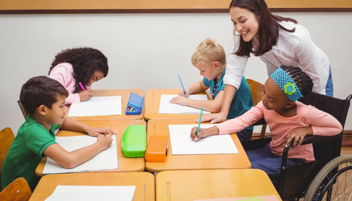 Happy teacher helping her students at the elementary school.