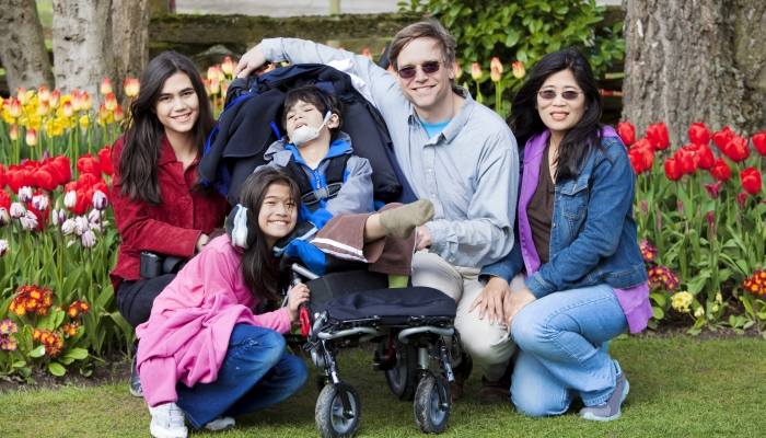 Interracial family sitting near disabled boy in wheelchair.