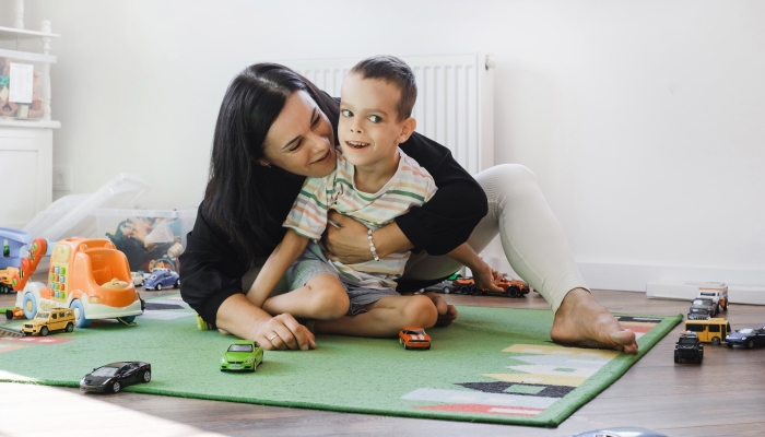 Kid with health problem playing toy cars with mother at home.