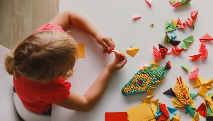 Little girl making origami crafts with paper.