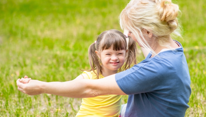 Little girl with syndrome down and her mother play together in a summer park.