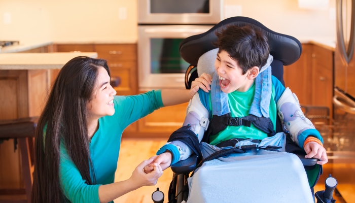 Nine year old disabled boy in wheelchair laughing with teen sister in kitchen.