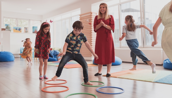 Nursery school children with female teacher on floor indoors in classroom.