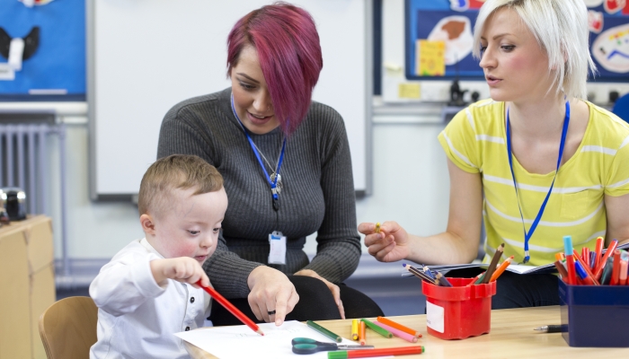 Nursery teacher sitting with a parent and her Down Syndrome son in the classroom.