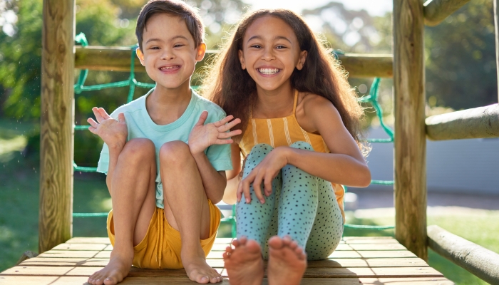 Portrait happy sister and brother with down syndrome on sunny playground equipment in summer backyard.